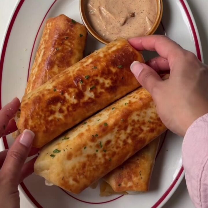 A crispy golden tortilla wrap sliced in half, showing juicy ground beef, melted cheddar, and pickles