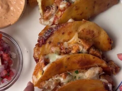 A stack of crispy golden mini tacos with melted cheese and chipotle chicken, served with a bowl of lime crema.