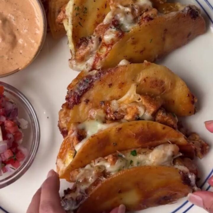 A stack of crispy golden mini tacos with melted cheese and chipotle chicken, served with a bowl of lime crema.