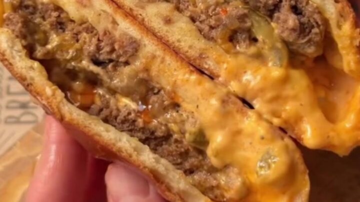 Golden baked stuffed cheeseburgers on a baking sheet, with sesame seeds and a glossy crust.