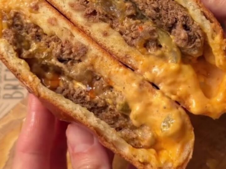 Golden baked stuffed cheeseburgers on a baking sheet, with sesame seeds and a glossy crust.