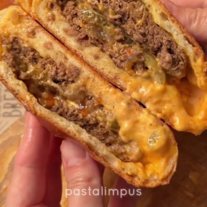 Golden baked stuffed cheeseburgers on a baking sheet, with sesame seeds and a glossy crust.