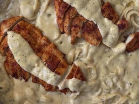 A fork twirling creamy lemon garlic fettuccine topped with sliced golden chicken breast