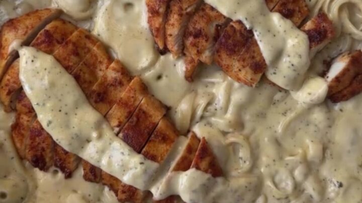 A fork twirling creamy lemon garlic fettuccine topped with sliced golden chicken breast