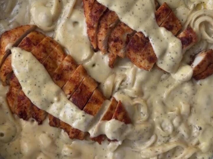 A fork twirling creamy lemon garlic fettuccine topped with sliced golden chicken breast