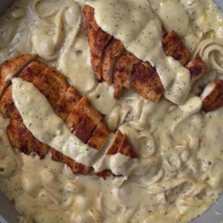 A fork twirling creamy lemon garlic fettuccine topped with sliced golden chicken breast