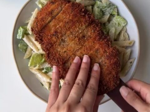 Crispy chicken Caesar pasta salad in a large bowl with golden chicken strips, bowtie pasta, romaine, tomatoes