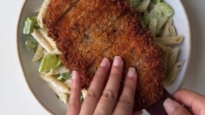 Crispy chicken Caesar pasta salad in a large bowl with golden chicken strips, bowtie pasta, romaine, tomatoes