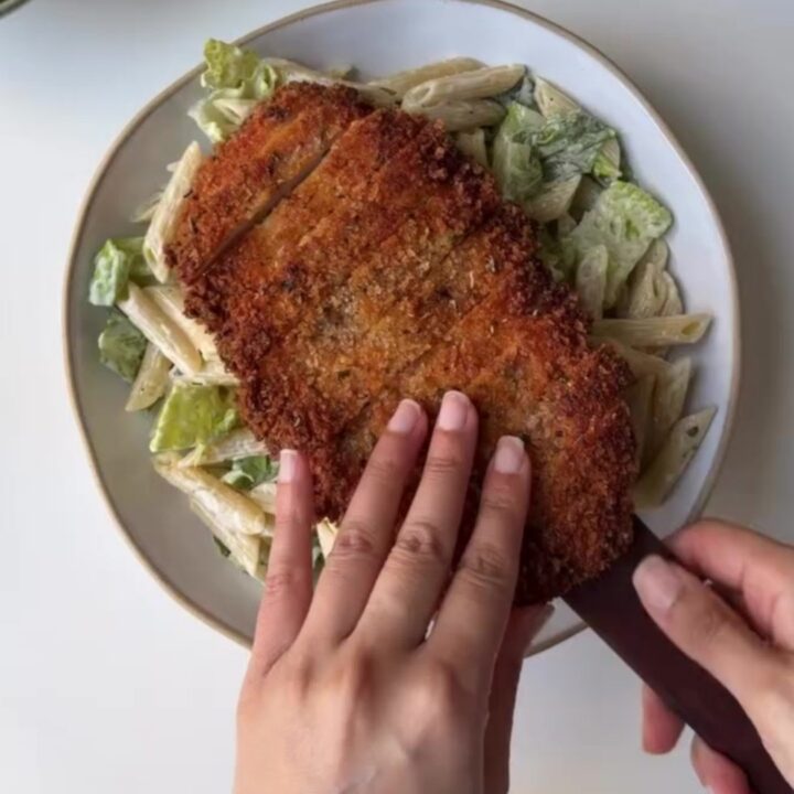 Crispy chicken Caesar pasta salad in a large bowl with golden chicken strips, bowtie pasta, romaine, tomatoes