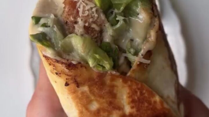 Crispy chicken Caesar wrap cut in half showing golden chicken, romaine, and parmesan