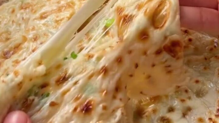 Golden Turkish flatbread folded in half with melted cheese and scallions spilling out.