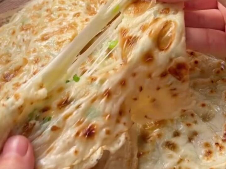 Golden Turkish flatbread folded in half with melted cheese and scallions spilling out.