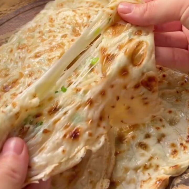 Golden Turkish flatbread folded in half with melted cheese and scallions spilling out.