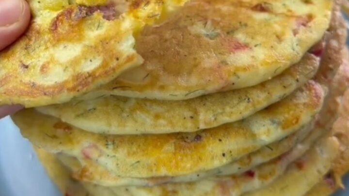 Golden brown XXL savory pancake on a wooden board, cut into wedges, with melted cheese and sausage visible.
