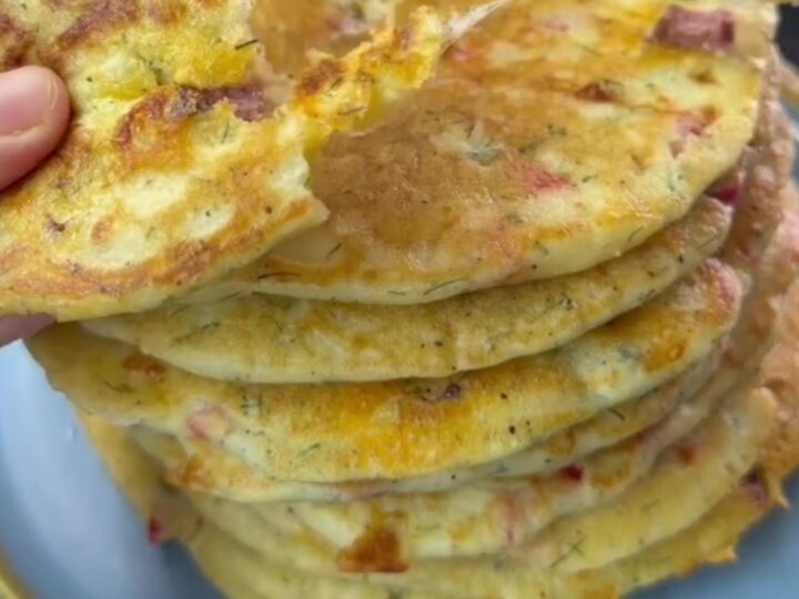 Golden brown XXL savory pancake on a wooden board, cut into wedges, with melted cheese and sausage visible.
