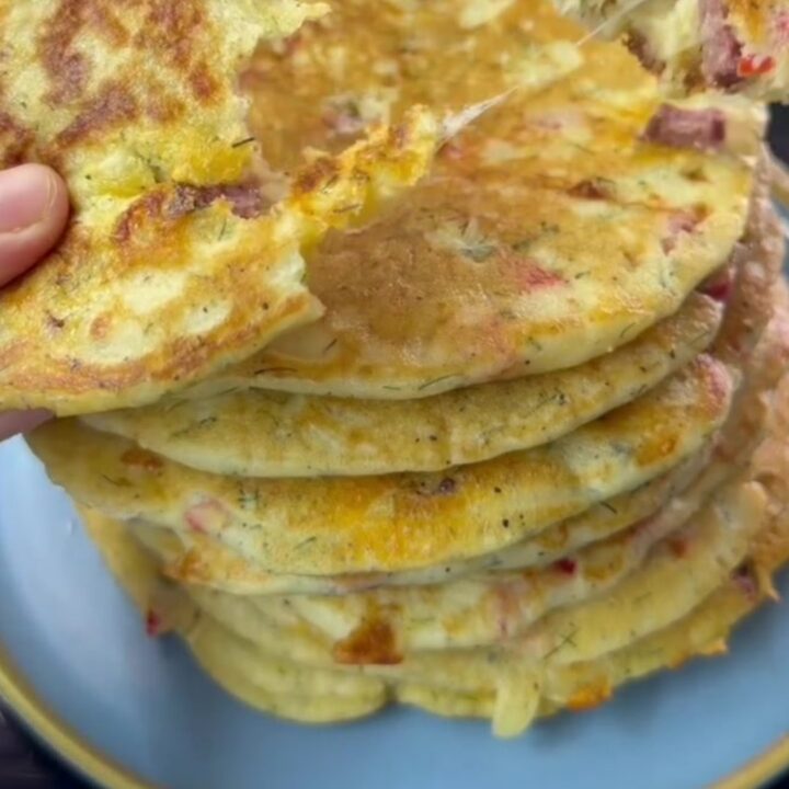 Golden brown XXL savory pancake on a wooden board, cut into wedges, with melted cheese and sausage visible.
