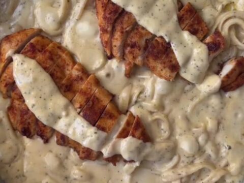 A plate of lemon garlic chicken Alfredo with sliced chicken and parsley on top
