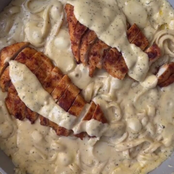 A plate of lemon garlic chicken Alfredo with sliced chicken and parsley on top
