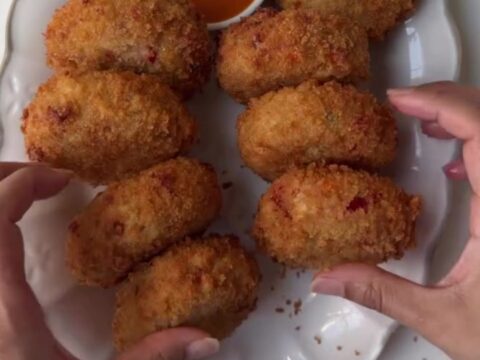 Golden-brown chicken mozzarella croquettes stacked on a wire rack with a bowl of creamy chipotle garlic dip.