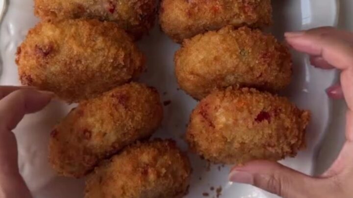Golden-brown chicken mozzarella croquettes stacked on a wire rack with a bowl of creamy chipotle garlic dip.