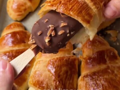 Golden flaky croissants on a baking sheet, one broken open showing airy layers