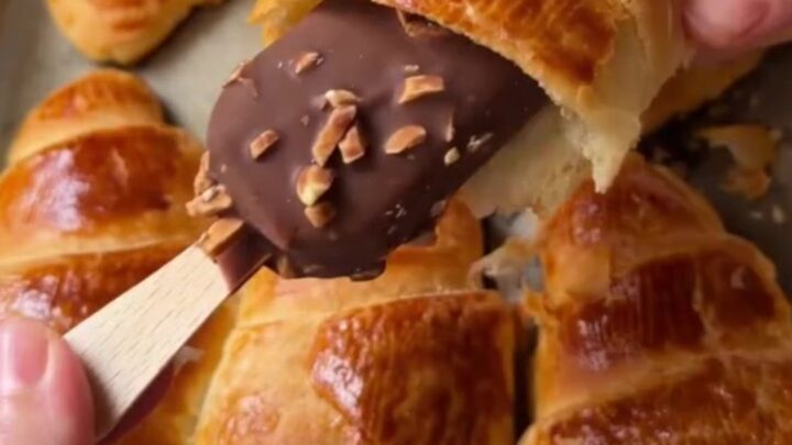 Golden flaky croissants on a baking sheet, one broken open showing airy layers