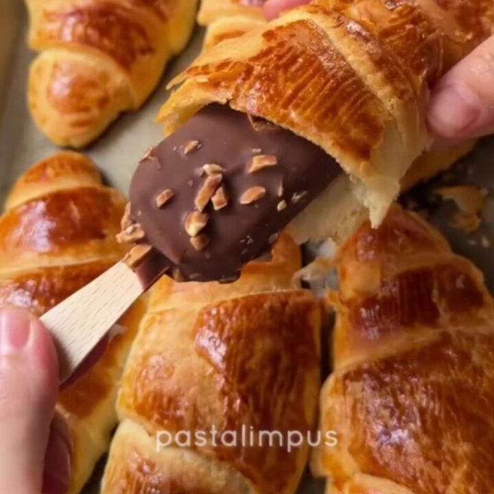 Golden flaky croissants on a baking sheet, one broken open showing airy layers