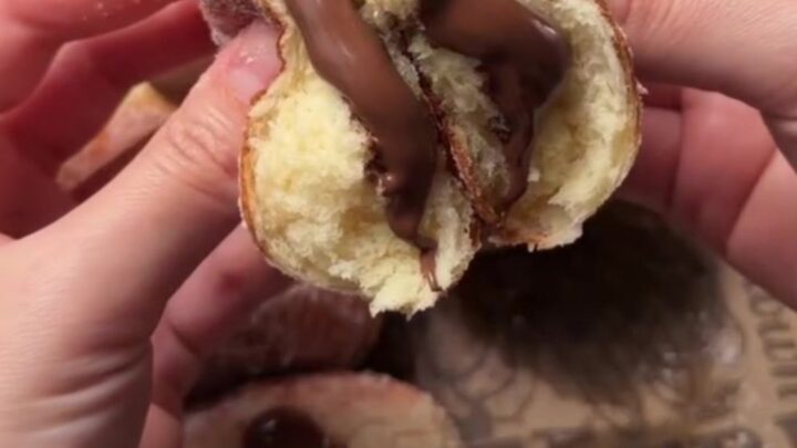 Golden sugar-dusted Berliner donut with strawberry jam oozing from the center