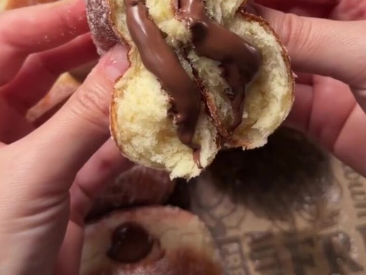 Golden sugar-dusted Berliner donut with strawberry jam oozing from the center