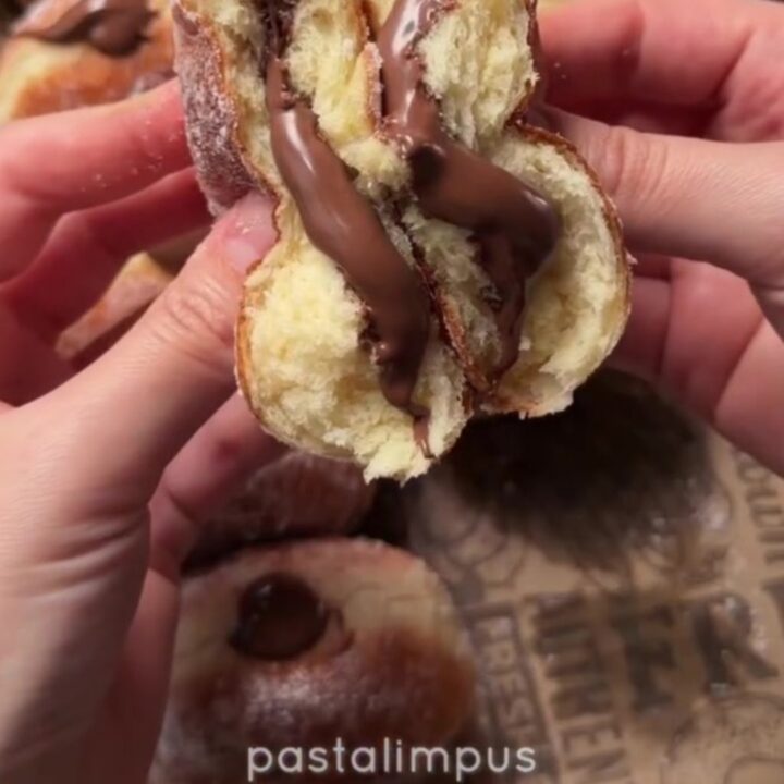 Golden sugar-dusted Berliner donut with strawberry jam oozing from the center