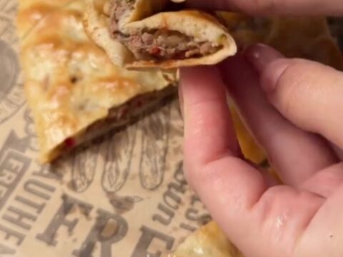 A golden, blistered Turkish pide with melted cheese and spiced beef, cut into slices on a wooden board.