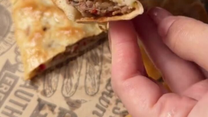 A golden, blistered Turkish pide with melted cheese and spiced beef, cut into slices on a wooden board.
