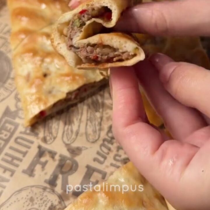 A golden, blistered Turkish pide with melted cheese and spiced beef, cut into slices on a wooden board.