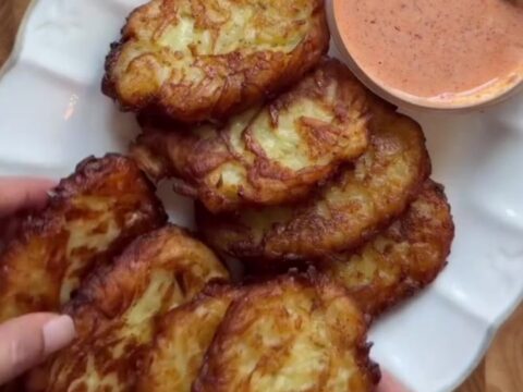 Golden crispy garlic parmesan hashbrowns stacked on a plate with a bowl of spicy mayo for dipping.