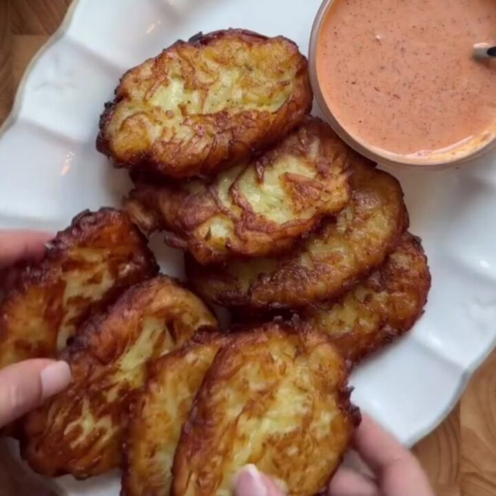 Golden crispy garlic parmesan hashbrowns stacked on a plate with a bowl of spicy mayo for dipping.