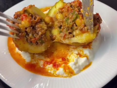 Braised stuffed round zucchini bowls topped with garlic yogurt and red pepper oil, in a shallow bowl with tomato sauce