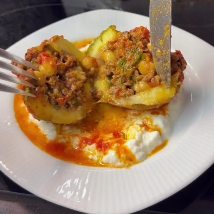 Braised stuffed round zucchini bowls topped with garlic yogurt and red pepper oil, in a shallow bowl with tomato sauce