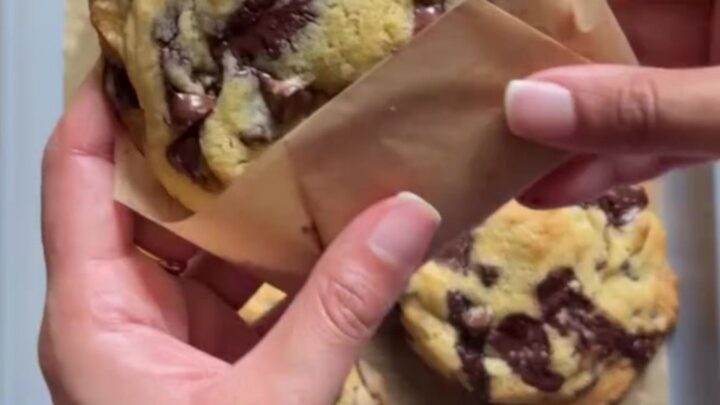 Tall gooey chocolate chip cookies on a cooling rack, with molten chocolate oozing from the center
