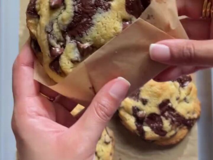 Tall gooey chocolate chip cookies on a cooling rack, with molten chocolate oozing from the center