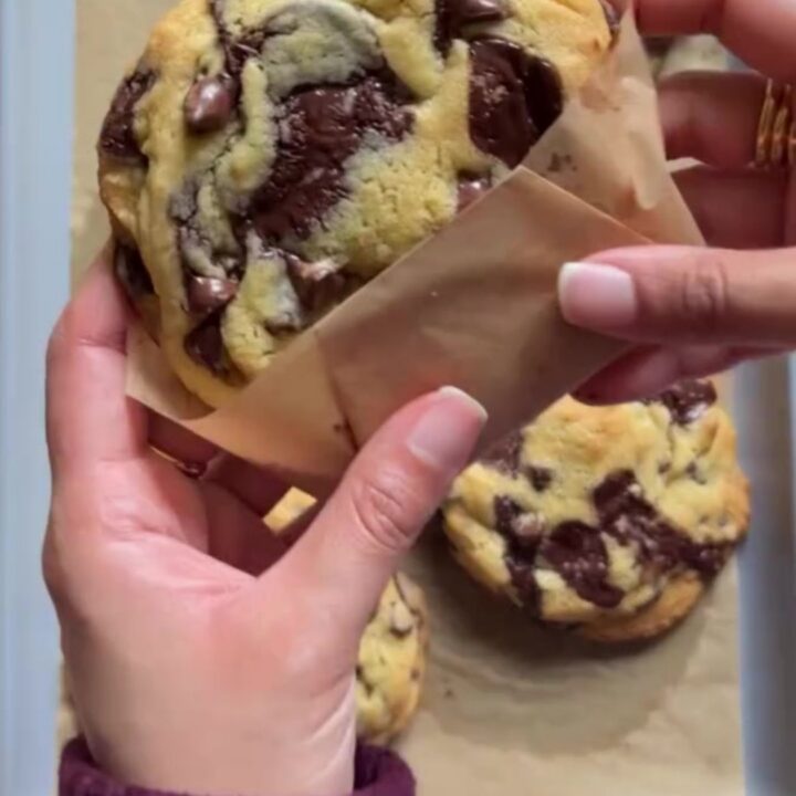 Tall gooey chocolate chip cookies on a cooling rack, with molten chocolate oozing from the center