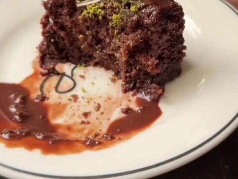 A slice of Islak Kek on a plate, showing the dark, glossy fudge-soaked sponge topped with crushed green pistachios.