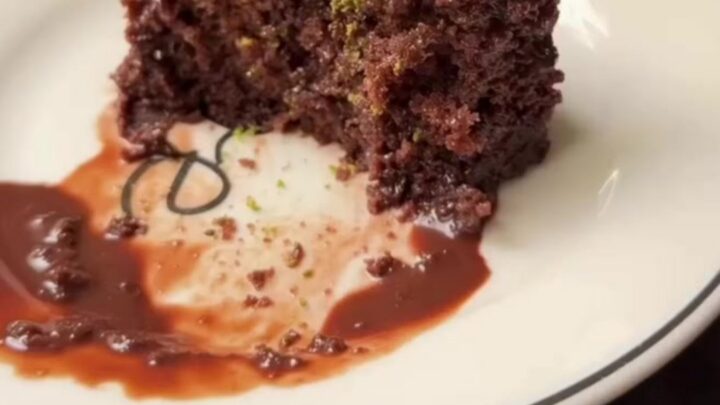 A slice of Islak Kek on a plate, showing the dark, glossy fudge-soaked sponge topped with crushed green pistachios.