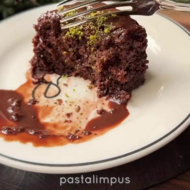 A slice of Islak Kek on a plate, showing the dark, glossy fudge-soaked sponge topped with crushed green pistachios.