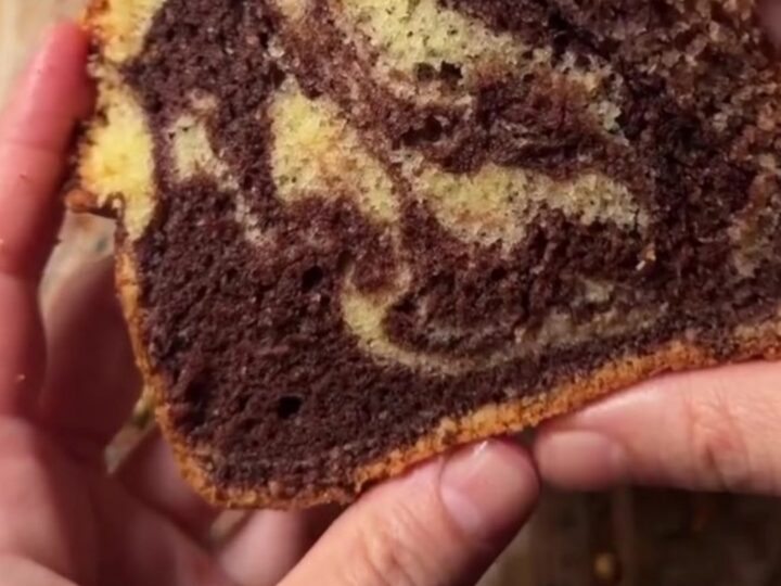 A golden marble loaf cake dusted with powdered sugar, showing a zebra swirl inside.