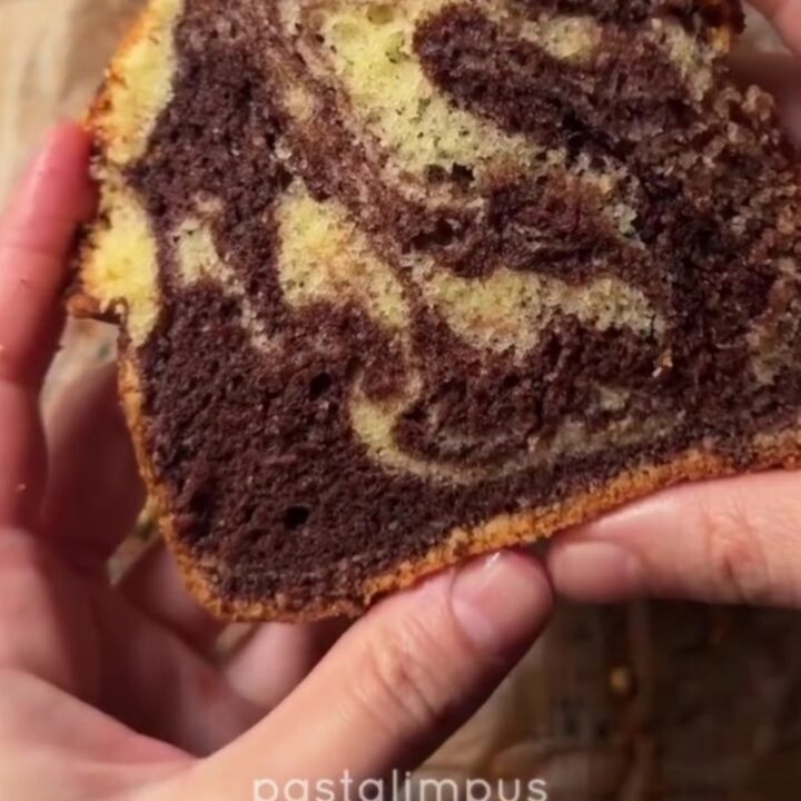 A golden marble loaf cake dusted with powdered sugar, showing a zebra swirl inside.