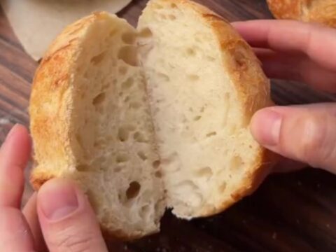 A blistered sourdough boule with a dark, crackling crust, cut open to show an airy honeycomb crumb.