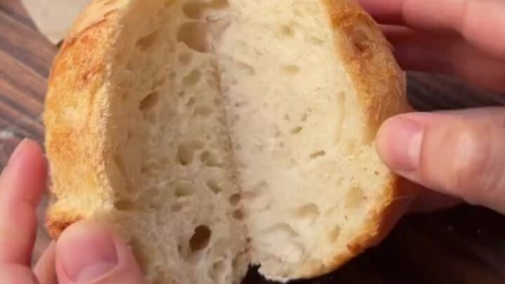 A blistered sourdough boule with a dark, crackling crust, cut open to show an airy honeycomb crumb.