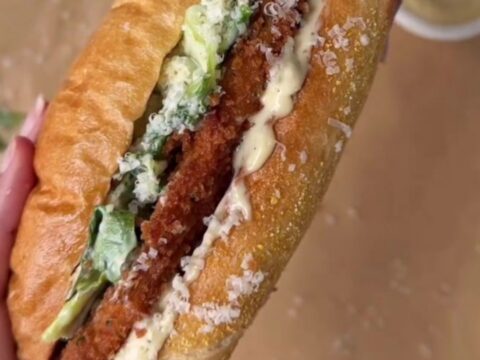 Crispy chicken Caesar sandwich on buttered brioche, cut in half showing layers of romaine, chicken, and Parmesan.