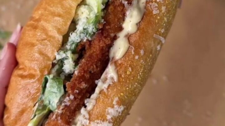 Crispy chicken Caesar sandwich on buttered brioche, cut in half showing layers of romaine, chicken, and Parmesan.