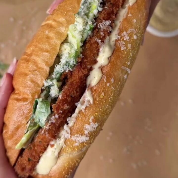 Crispy chicken Caesar sandwich on buttered brioche, cut in half showing layers of romaine, chicken, and Parmesan.
